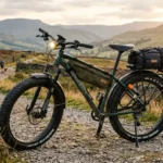 Rugged fat tyre electric bike on scenic UK trail with frame bag, pannier rack, and front light
